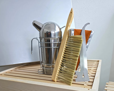 Imkereibedarf der Imkerei SIMI-S-IMI mit Edelstahl-Smoker, Stockmeißel mit Bienenbesen und Honig-Rähmchen auf einer Holzbeute bereitgelegt
